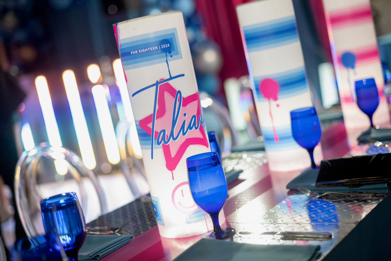 Blue wine glasses and a colorful menu on a table with blurred lights in the background