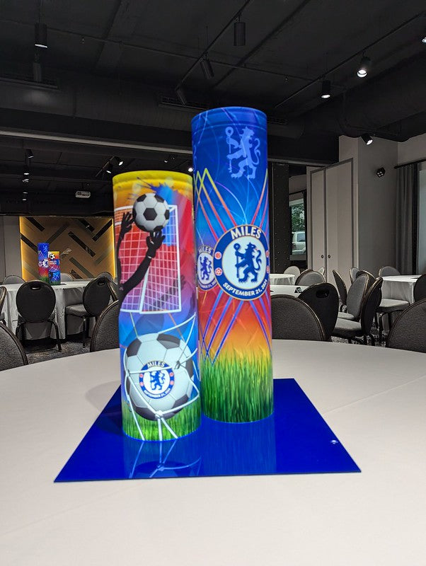 Two cylindrical promotional stands with soccer-themed designs on a table in an indoor setting.