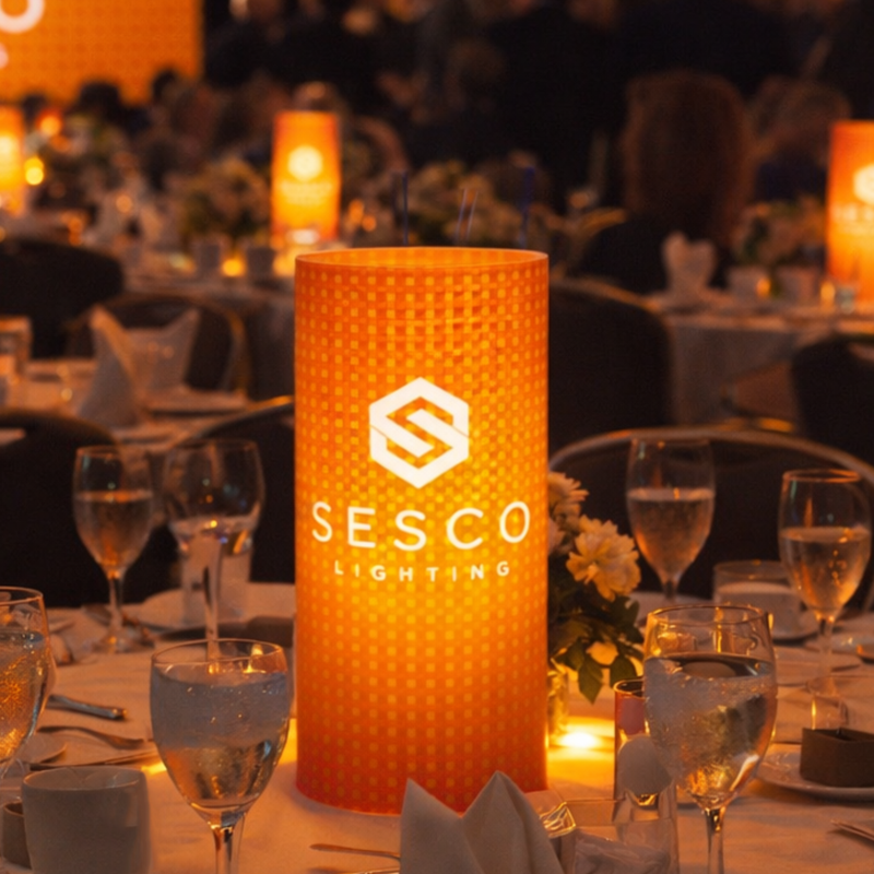 Orange textured lamp with 'Sesco Lighting' logo on a table setting with wine glasses and candles.