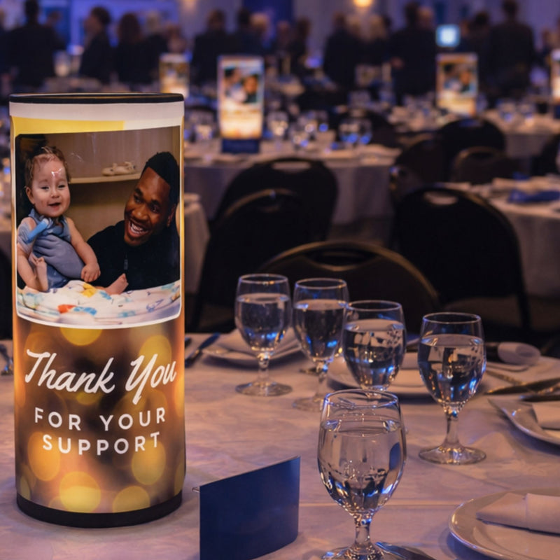Table setting with a 'Thank You for Your Support' card in the foreground, blurred event background