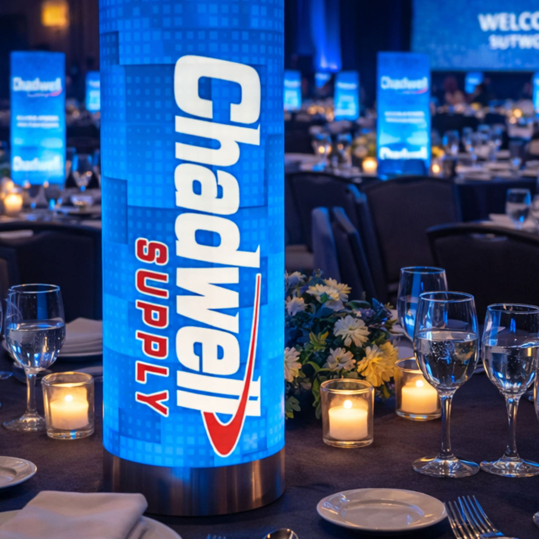 Lighted cylindrical sign with 'Chadwell Supply' branding on a table setting with glasses and candles.
